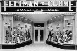 View of the Feltman and Curme shoe store at 610 16th (Sixteenth) Street in Denver, Colorado; shows footwear in display windows and a neon sign: "Feltman & Curme Quality Shoes."