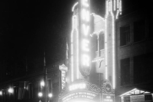 Night view of the 16th street entrance of the Denver Theater at 510 16th (Sixteenth) Street in Denver, Colorado; shows electric signs and the marquee: "Joan Crawford in Modern Maidens," and "Ted Hack in Say It With Music." Banner reads: "Cuba - U.S.A."