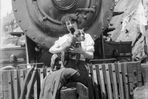 Singer and actress Anna Held is seated on the front of a train in Colorado Springs (El Paso County), Colorado. She holds a dog.