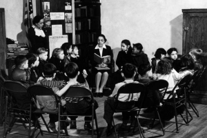 Interior view at the Community Vocational Center at the Cosmopolitan Branch of the Denver Public Library in Denver, Colorado; children listen to a Black (African American) woman read a story. Sign reads: "The Gold Star Reading Club."