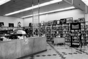 Interior view at Dahlia Branch of the Denver Public Library in Denver, Colorado; a Black (African American) man sits at the counter. Paintings top bookshelves.