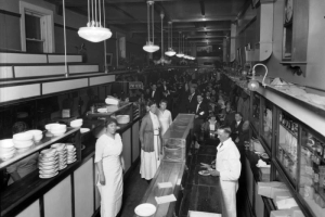 Interior view of Pell's Oyster House in Denver, Colorado; shows men, women, dishes, light fixtures, and a sign: "Pay Here."