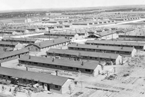 Overview of prefabricated army-style barracks at the Granada Relocation Center, Camp Amache, Prowers County, southeastern Colorado, includes small trees and gardens with rolling prairie in the background.