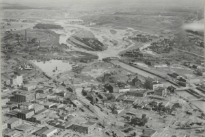 Aerial view of a flooded Arkansas River, damaged buildings and rail yards in Pueblo (Pueblo County), Colorado. Shows the Pueblo Smelter, the Nuckolls Packing Company building, standing water identified as "Death Lake", a flooded Missouri Pacific Railway Company rail yard, Denver and Rio Grande Western and Atchison, Topeka and Santa Fe railroad bridges, and City Hall with a domed cupola.