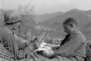 Taken during the Italian campaign, the photograph shows two Tenth  Mountain Division soldiers relaxing in a haystack by reading magazines. In  the background are mountains and leafless trees.