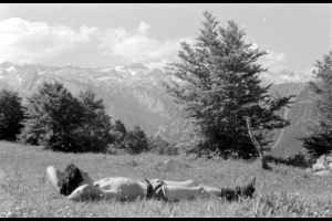 After the end of the war the Tenth Mountain Division was posted in Yugoslavia to defend U.S. interests over the partition of the Italian - Austrian - Yugoslavian border. This duty left the men with ample time to relax. Pictured is a man wearing only shorts and hiking boots, lying in a grassy field with rugged, snow-capped mountains in the distance.