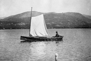 Henry Hanington and a dog on one of the first sailboats on Grand Lake (Grand County),Colorado, framed by mountain ridges on the horizon.