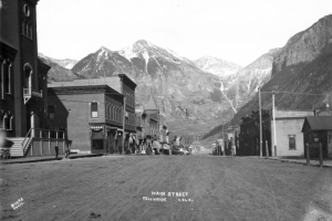 View east down Main Street (Colorado Avenue) Telluride (San Miguel County), Colorado. Ajax, Telluride and Ingram Peaks with light snow and Ingram Falls are in background. Buildings include the San Miguel County Courthouse, the Sheridan Hotel; First National Bank, and the Telluride Mercantile Company block.