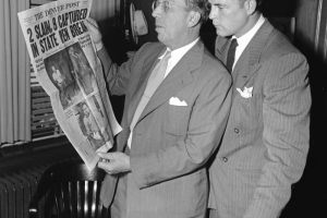 Scott Brady, star of "Canon City," and Palmer Hoyt, editor and publisher of the Denver Post from 1946-1971, with a Denver Post newspaper, look at the headlines in an office in Denver, Colorado. A sheet with "The Denver Post Deadline Schedule" sits on the desk. The headline, about the 1947 prison break on which "Canon City" was based, reads: "2 Slain, 9 Captured, In State Pen Break, Stir Crazy Cons Lead Pen Break."