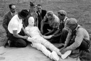 Men engage in first aid instruction in Denver, Colorado; the "victim" is wrapped in bandages.