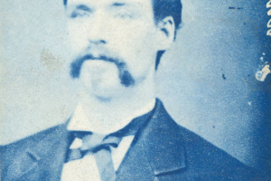 Studio portrait of Patrick McCann, an employee in a reduction works in Georgetown (Clear Creek County), Colorado. He wears a coat with bound, wide lapels, a vest, a shirt with an upright collar and a bow tie. His dark hair is parted on the side and combed into a cowlick. He has a long mustache.