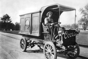 Theo Koch drives an Adolph Coors Golden Brewery delivery truck, in Golden, Jefferson County. The wood panel Frayer - Miller truck has the steering wheel on the right side, narrow tires and lantern headlights.