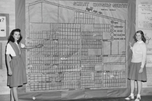 Girls pose by a wall-sized map of the Park Hill District at Smiley Junior High School, in Denver, Colorado. Lettering at the top reads: "Smiley Housing Survey, Park Hill District."