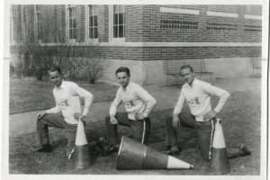 Three male cheerleaders from South High School in Denver, Colorado pose on one knee with their megaphone for a team picture. Taken at 1700 East Louisiana Avenue, Denver, Colorado, 80210.
