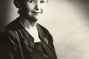 Portrait of Agnes Wright Spring, posing in a black blouse and holding a book.
